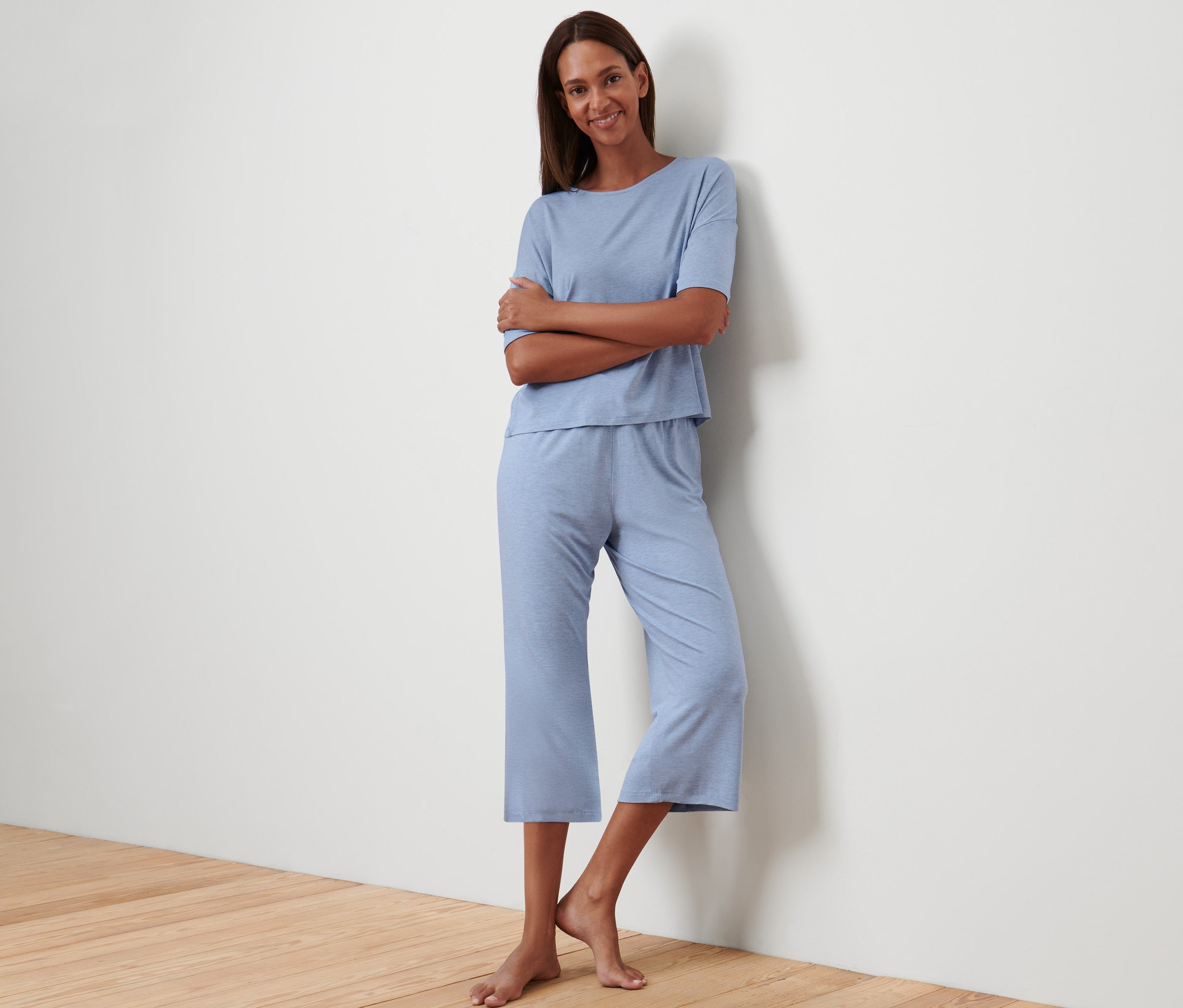 Eine Frau posiert an eine Wand gelehnt in einem blauen Pyjama in 3/4-Länge.