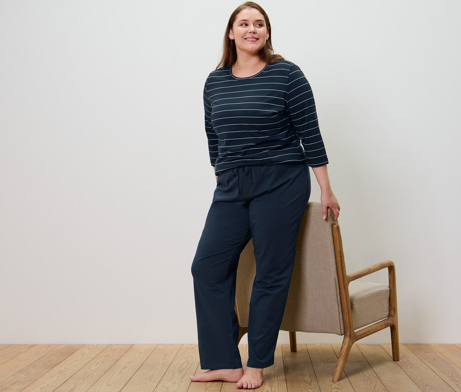 Frau im dunkelblauen gestreiften Pyjama steht neben einem Sessel.