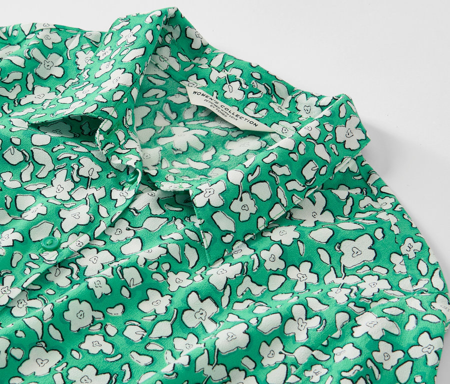 Detailansicht eines bedruckten Hemdblusenkleids mit grünem Grund und weißen Blumen.
