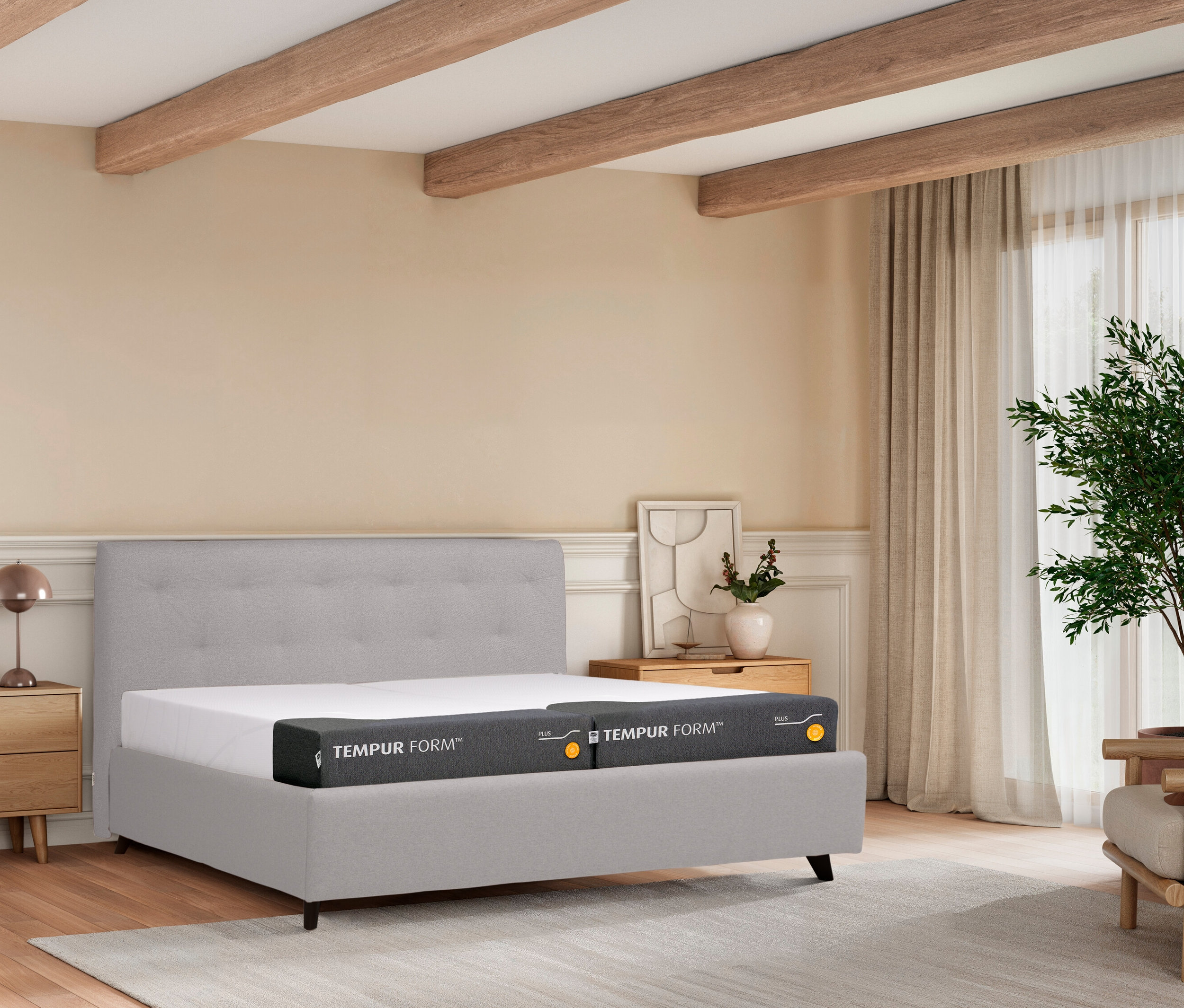 Schlafzimmer mit grauem Bett, Nachttisch, Lampe und Zimmerpflanze.