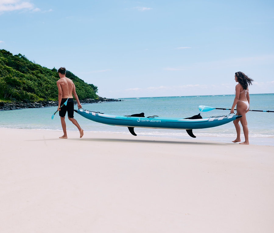 Ein Mann und eine Frau tragen ein Spinera Hybris 410 2-Personen-Kajak am Strand.
