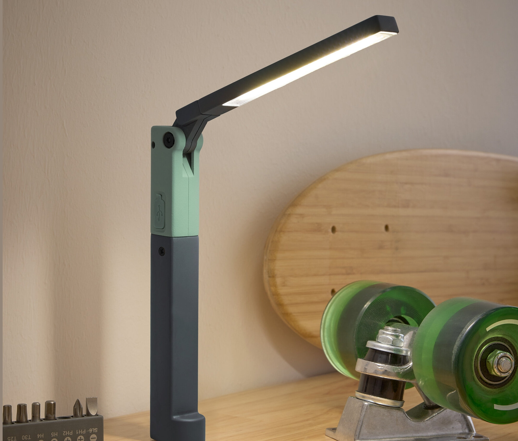 Eine LED-Arbeitsleuchte, ein Schraubenzieher, ein Bit-Set und Skateboard-Zubehör stehen auf einem Holztisch.
