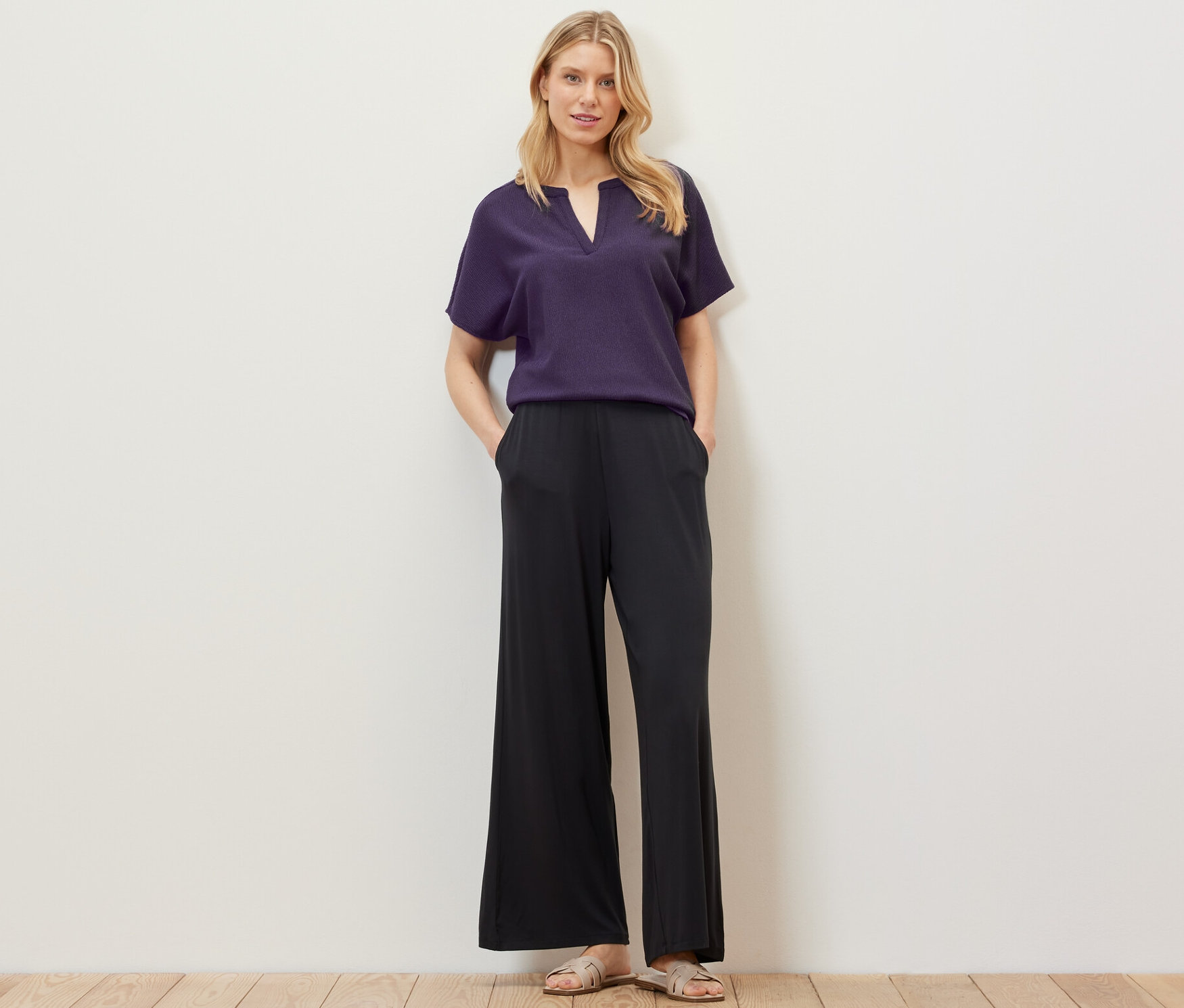 Blonde Frau posiert in strukturierter Kurzarmbluse und schwarzer Hose.