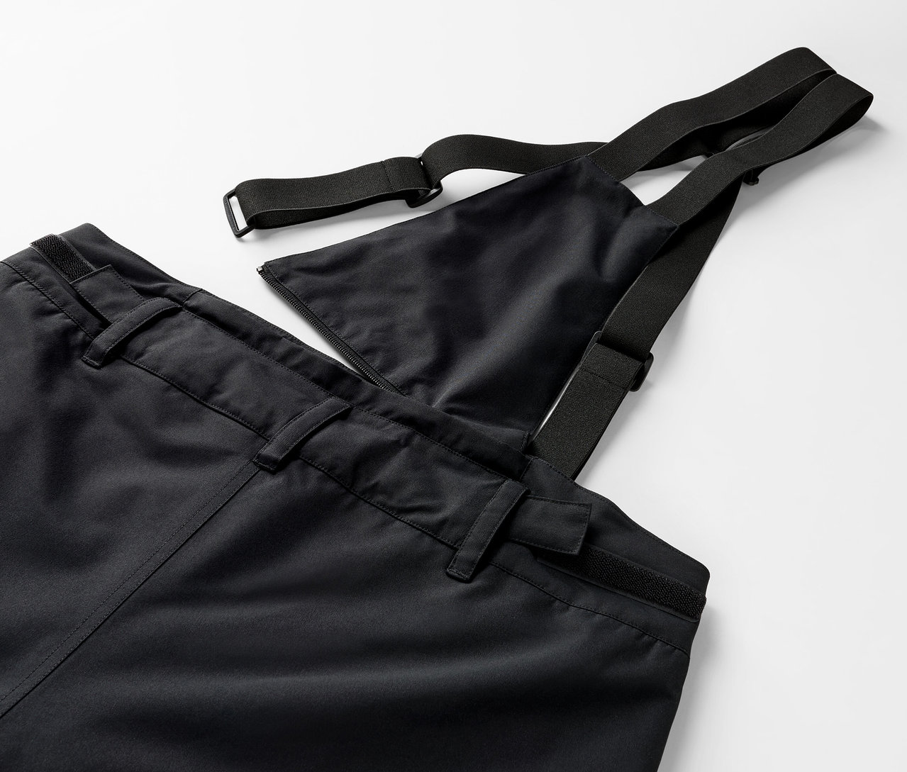 Detailaufnahme einer schwarzen Hose mit Latz und elastischen Trägern.