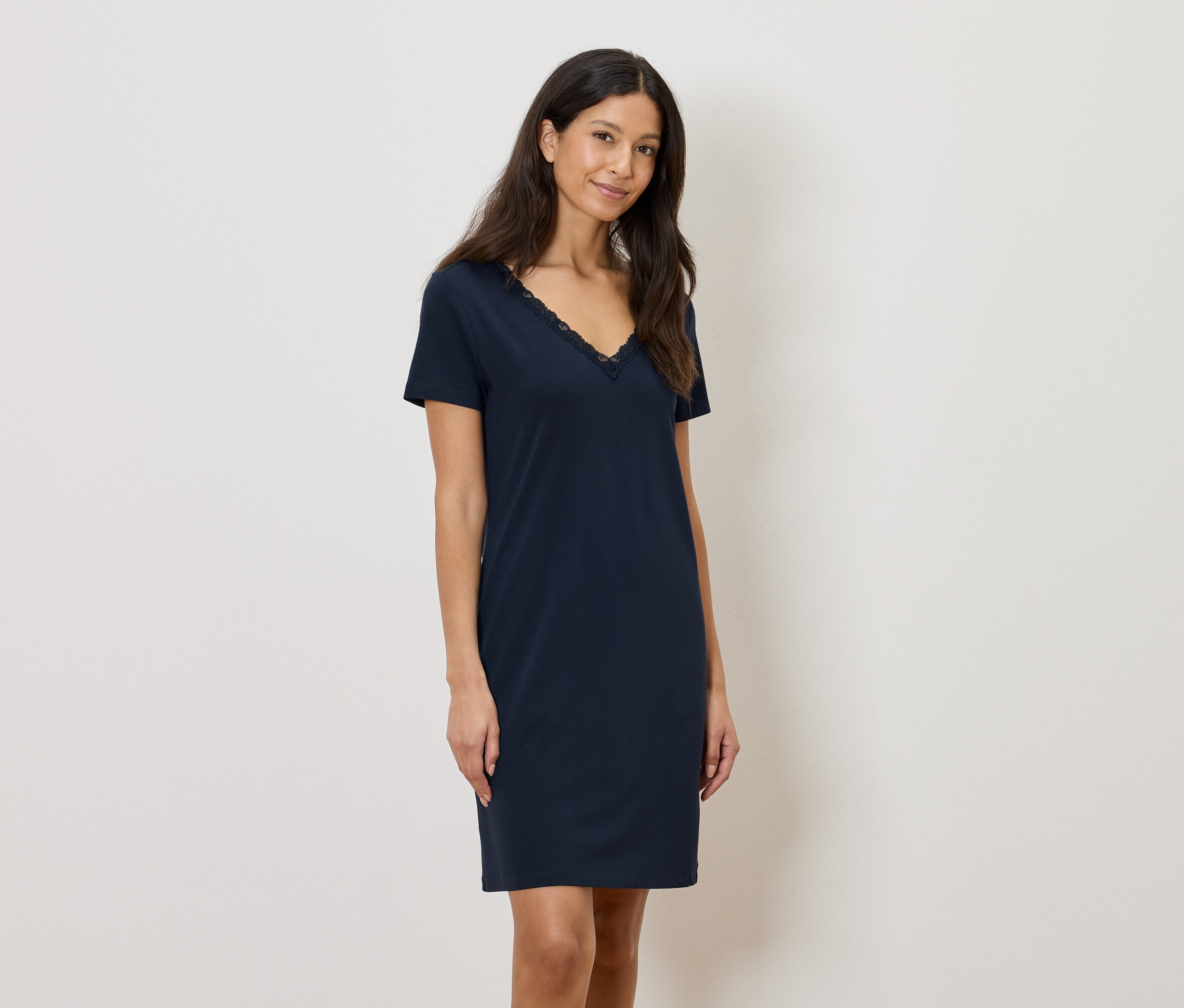Frau trägt ein dunkelblaues, knielanges Kleid mit Spitzenbesatz am V-Ausschnitt.