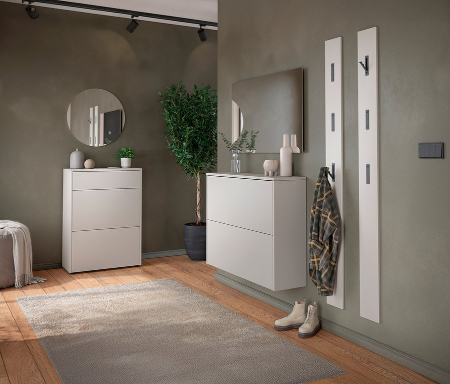 Eingangsbereich mit zwei weißen Schuhschränken, rundem Spiegel, Garderobenpaneelen, Teppich und Topfpflanze.