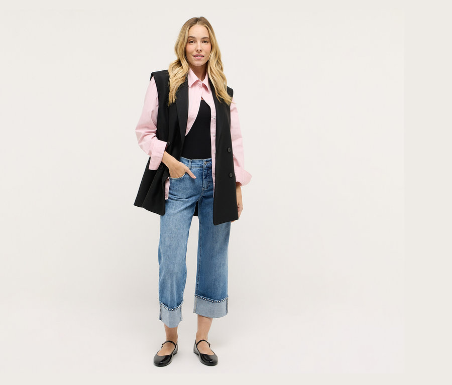 Frau mit schwarzer Weste, rosa Hemd, Jeans und schwarzen Schuhen.
