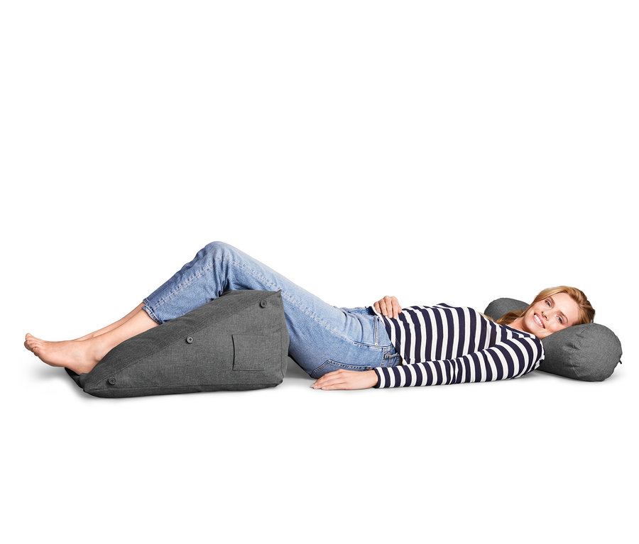 Frau liegt und benutzt ein Rückenkissen mit Nackenrolle.