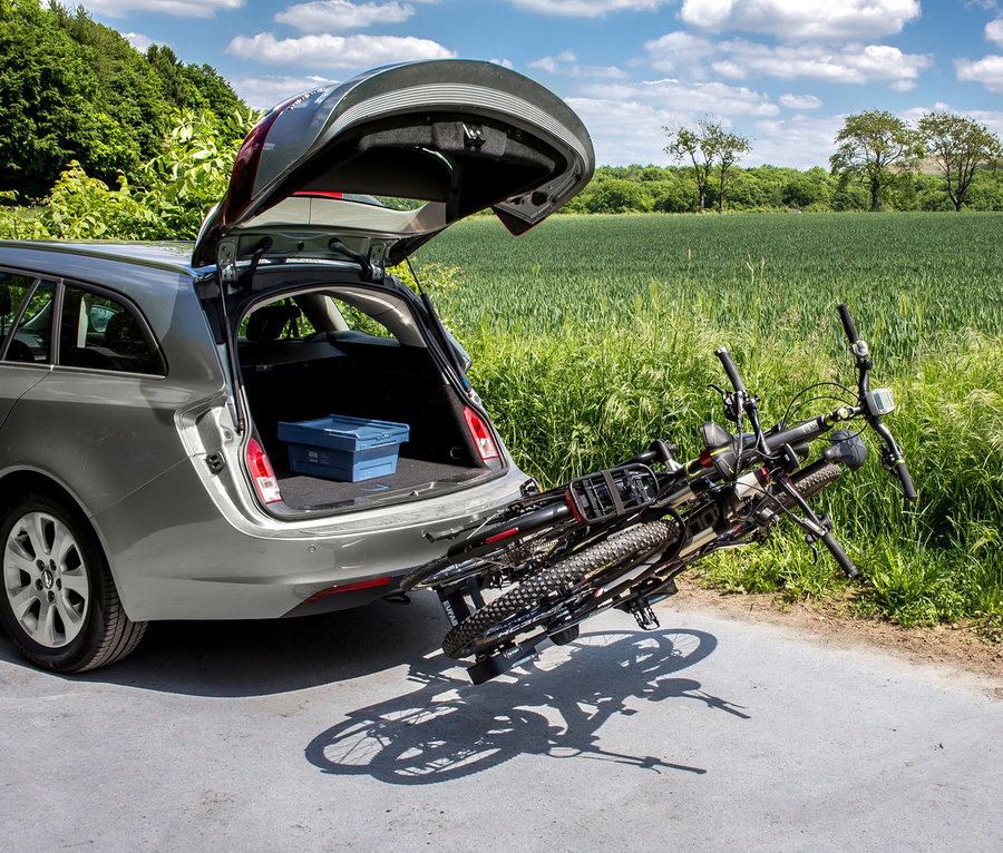 Ein silberner Kombi hat die Heckklappe geöffnet, im Kofferraum befindet sich eine blaue Kiste. Auf der Anhängerkupplung ist ein »Premium 2« Fahrradträger mit zwei Fahrrädern montiert.