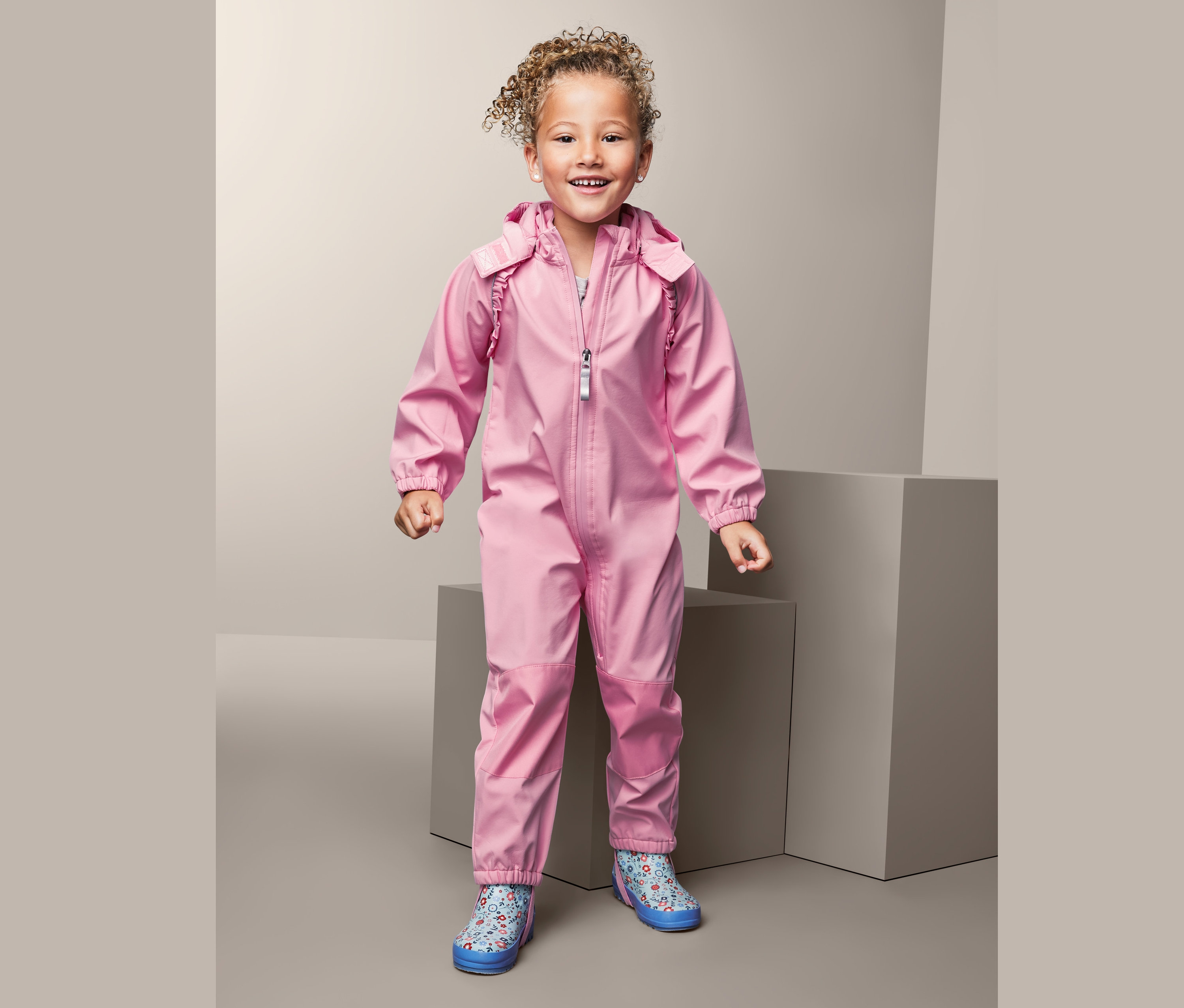 Lächelndes Mädchen im rosafarbenen Softshell-Einteiler aus recyceltem Material.