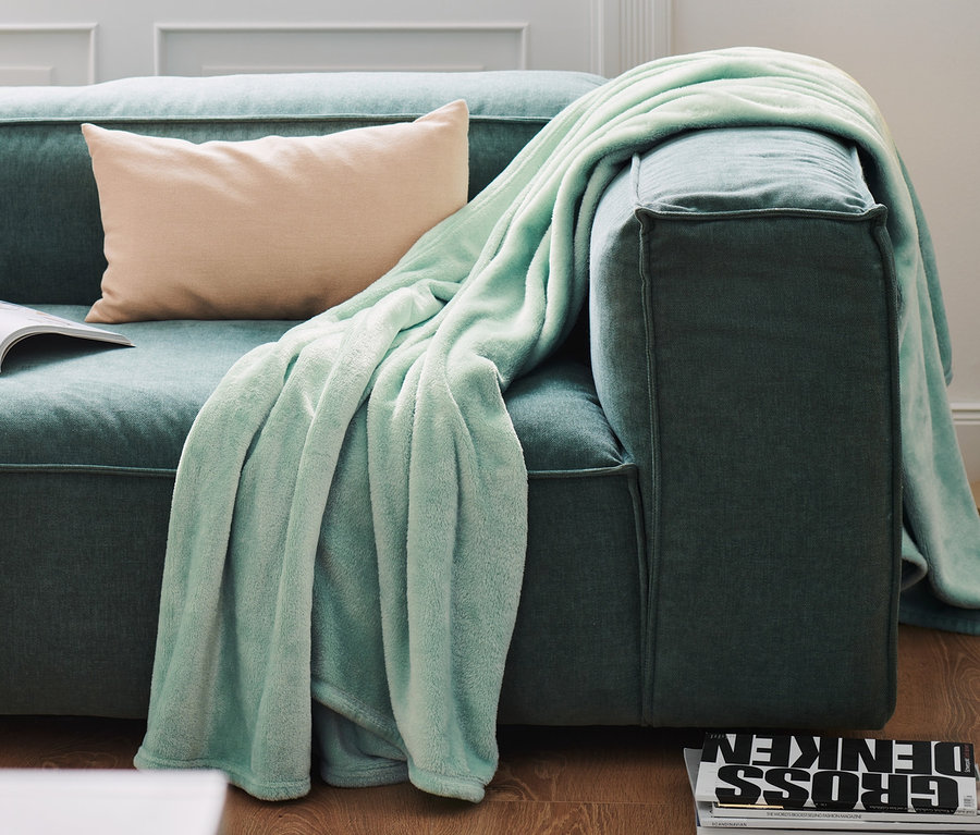 Eine Kuscheldecke und ein Kissen liegen auf einem Sofa.