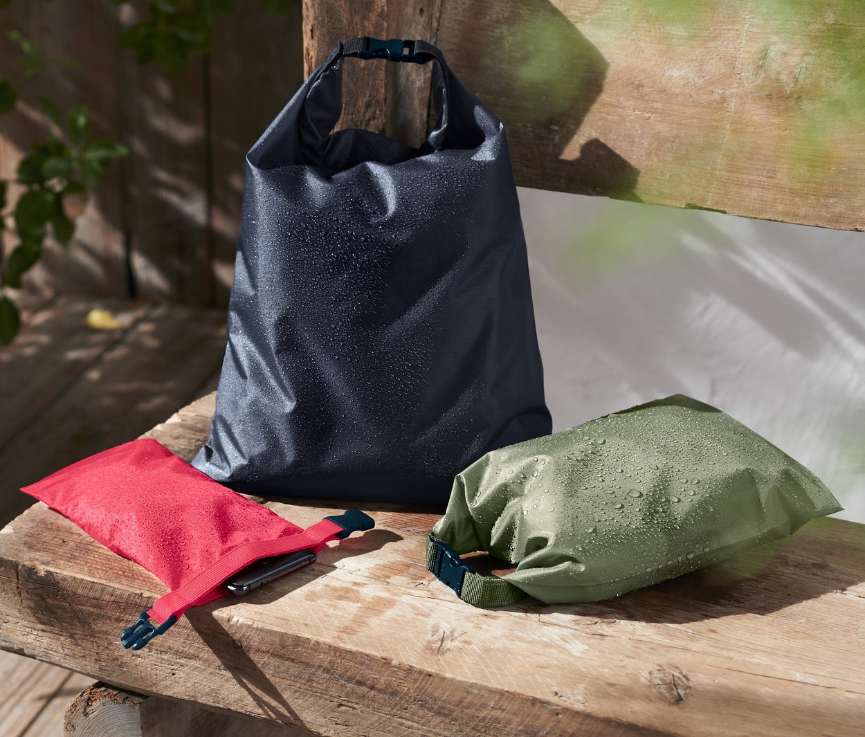 Drei wasserfeste Packsäcke liegen auf einer Holzbank.