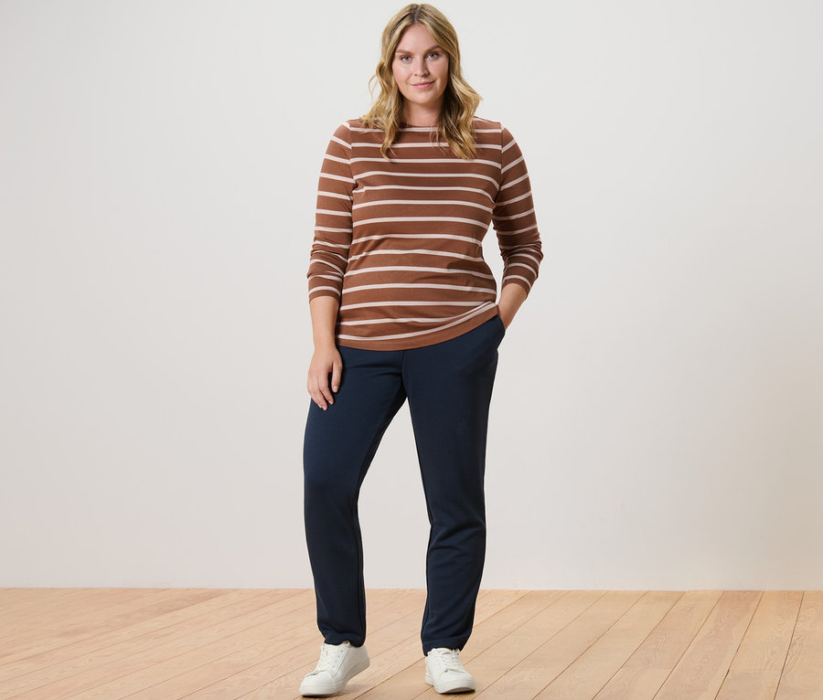 Frau posiert in gestreiftem Langarmshirt, Cognac, und Joggpants.