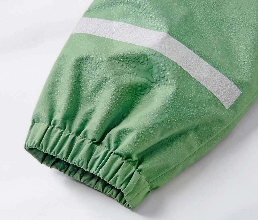 Detail einer Kinder-Regenhose in Grasgrün mit reflektierendem Streifen und Wassertropfen.
