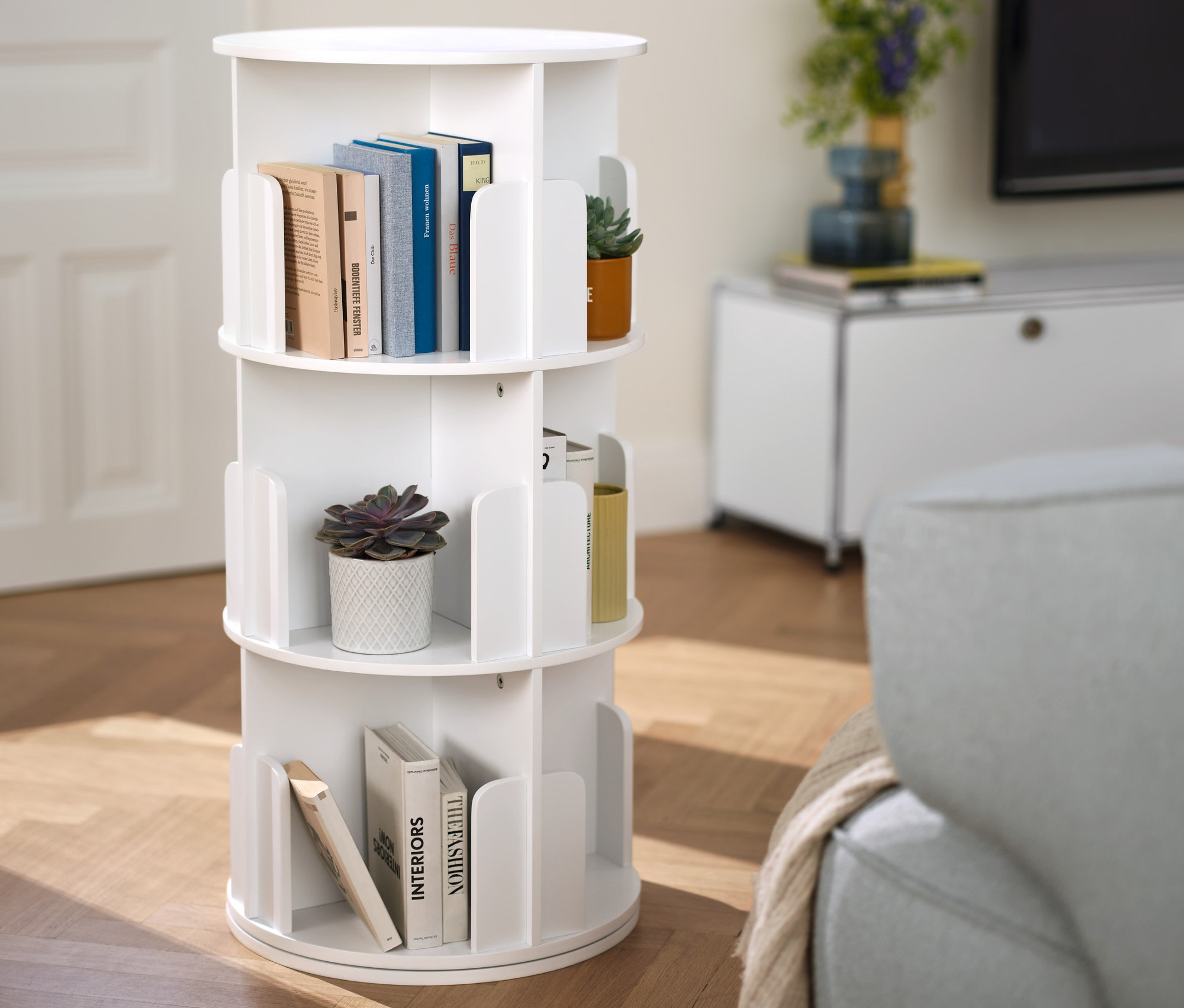 Im Vordergrund drehbares Bücherregal mit Büchern und Pflanzen. Im Hintergrund Lowboard Metall »CN3« mit Schubladen, weiß.
