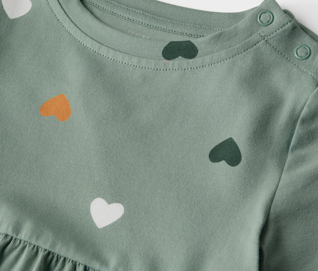 Detailaufnahme eines hellgrünen Kinder-Jerseykleids mit Herzprint und Knöpfen an der Schulter.