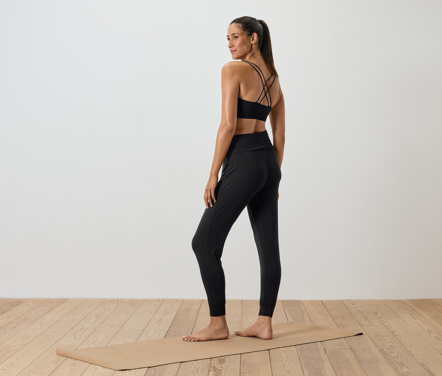 Frau in schwarzer Sportbekleidung steht auf einer Yogamatte.