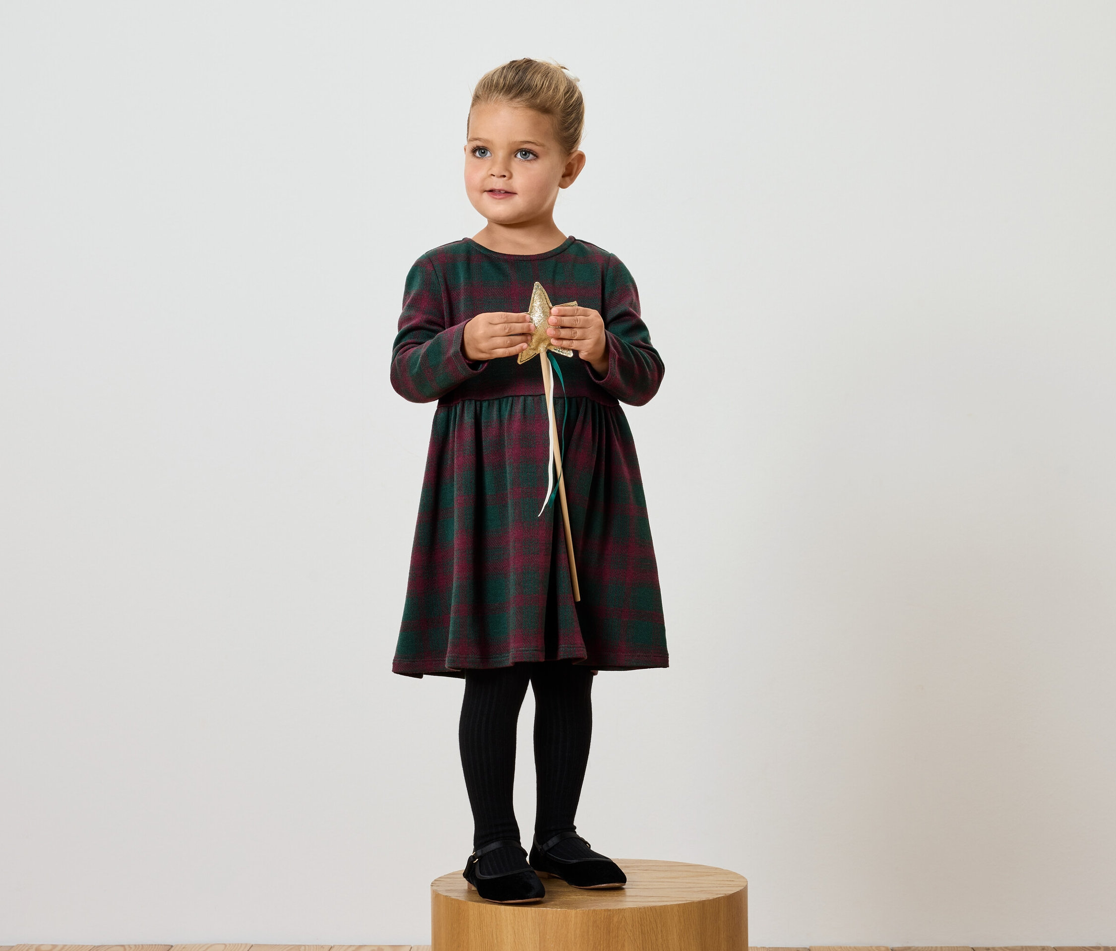Mädchen im karierten Kleid hält goldenen Stern.