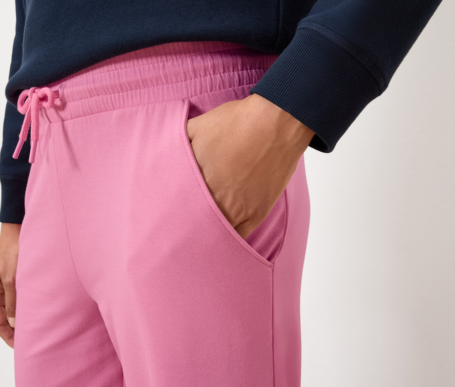 Detailaufnahme einer Frau, die eine rosafarbene Jogginghose trägt und ihre Hand in der Tasche hat.
