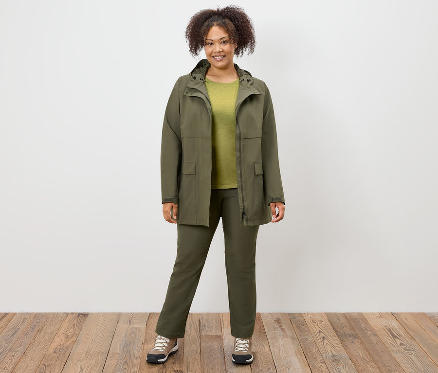 Frau steht in olivgrünem Mantel, Hose und Schuhen.