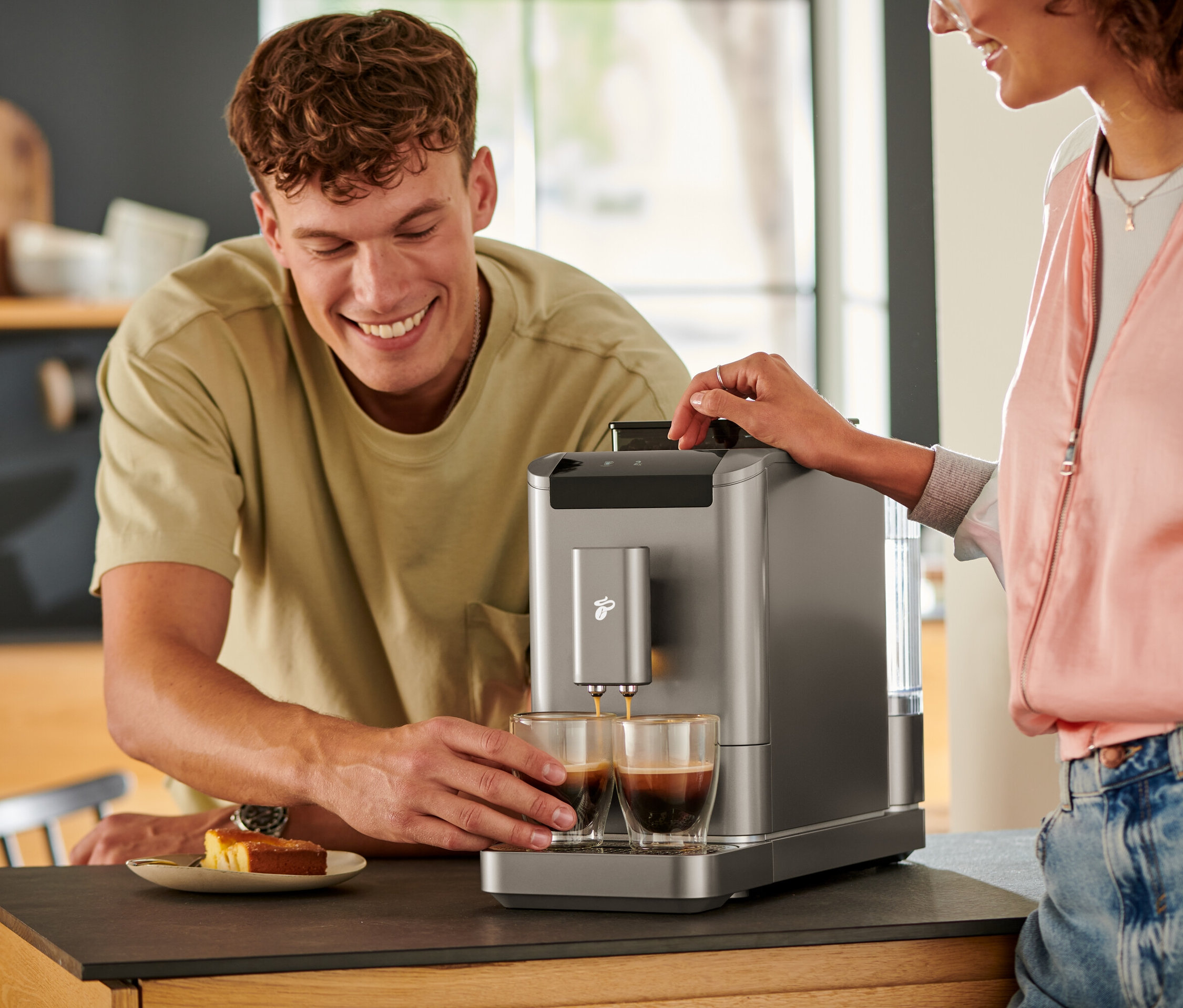 Ein Mann schaut zu, wie Kaffee aus einem »Esperto2 Caffè« Kaffeevollautomaten in Titanium Silver in zwei Gläser gegossen wird.
