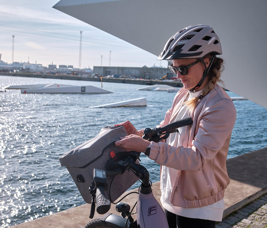 Frau befestigt FISCHER Lenkertasche PLUS Cita an einem Fahrrad vor dem Wasser.