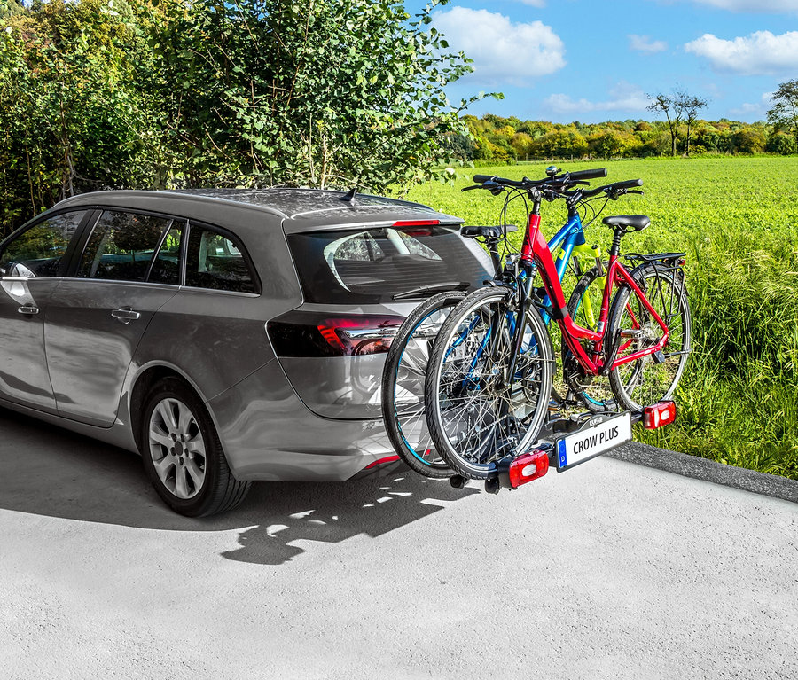 Grauer Kombi mit »CROW Plus« Fahrradträger und drei Fahrrädern auf einer Landstraße.
