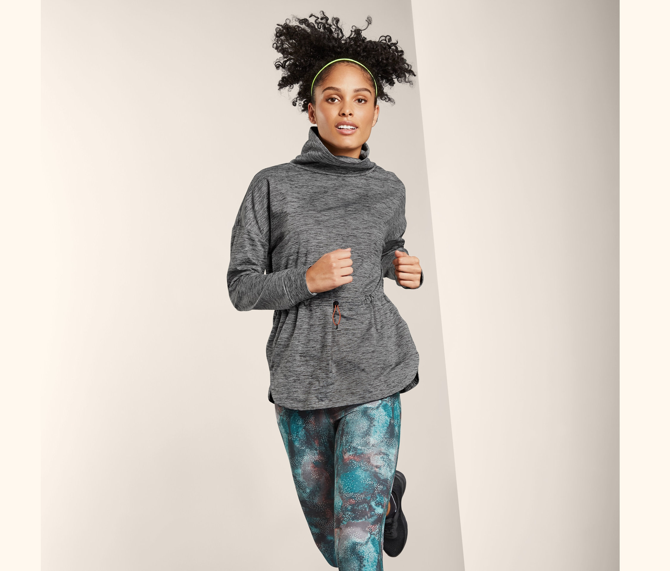 Eine Frau im Laufschritt trägt einen Thermo-Funktionssweater, bunte Leggings und schwarze Turnschuhe.