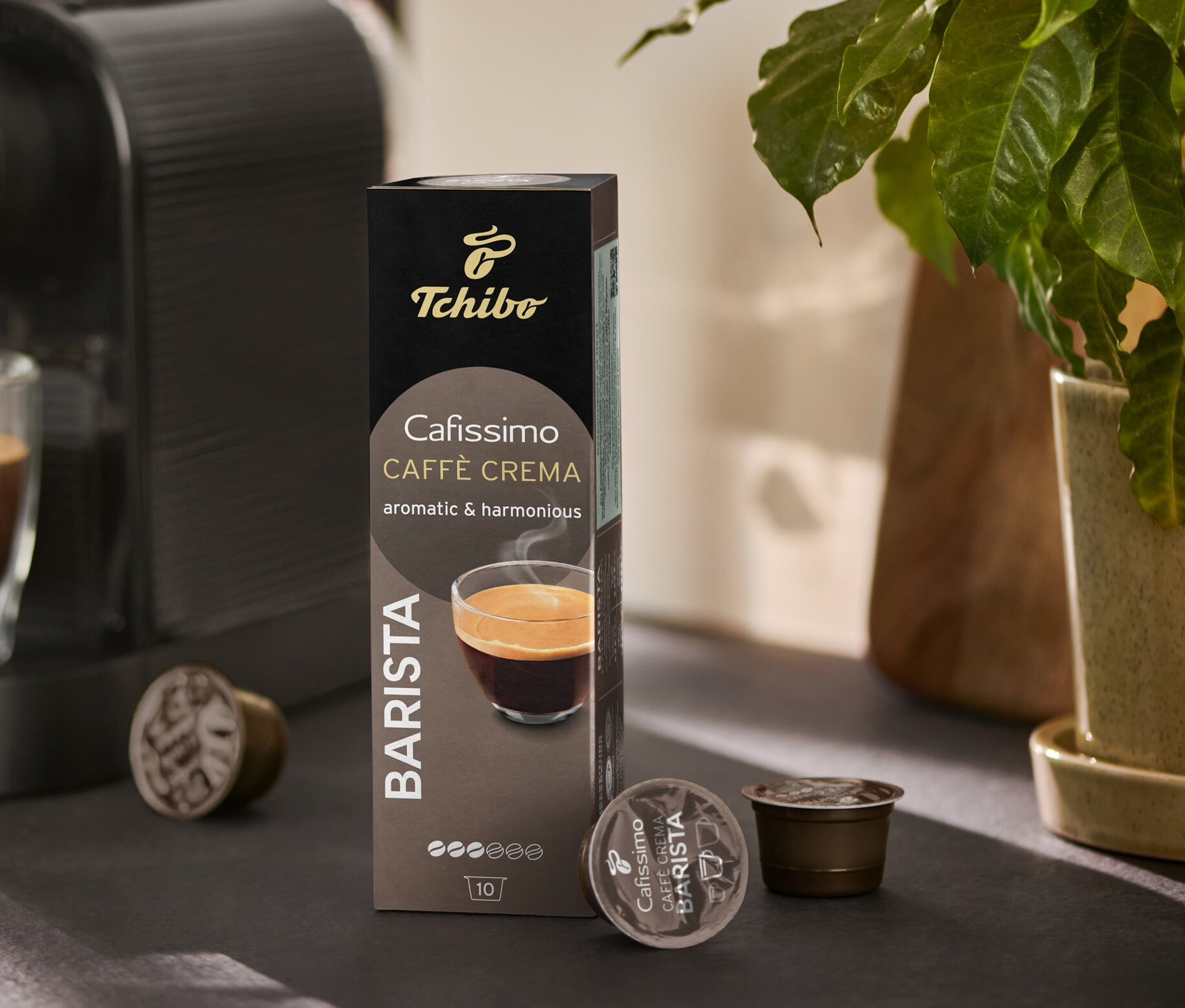 Kaffeemaschine füllt ein Glas mit Kaffee. Daneben stehen eine Packung Cafissimo BARISTA Caffè Crema und ein paar Kapseln.