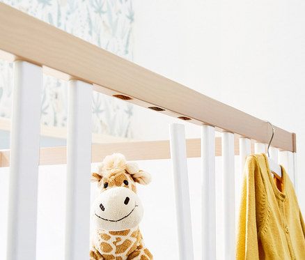 Detailansicht eines Kinderbetts mit einem Stofftier-Giraffe und einer gelben Strickjacke, Teil des 3-teiligen, großen Pinolino Sets »Light« breit.