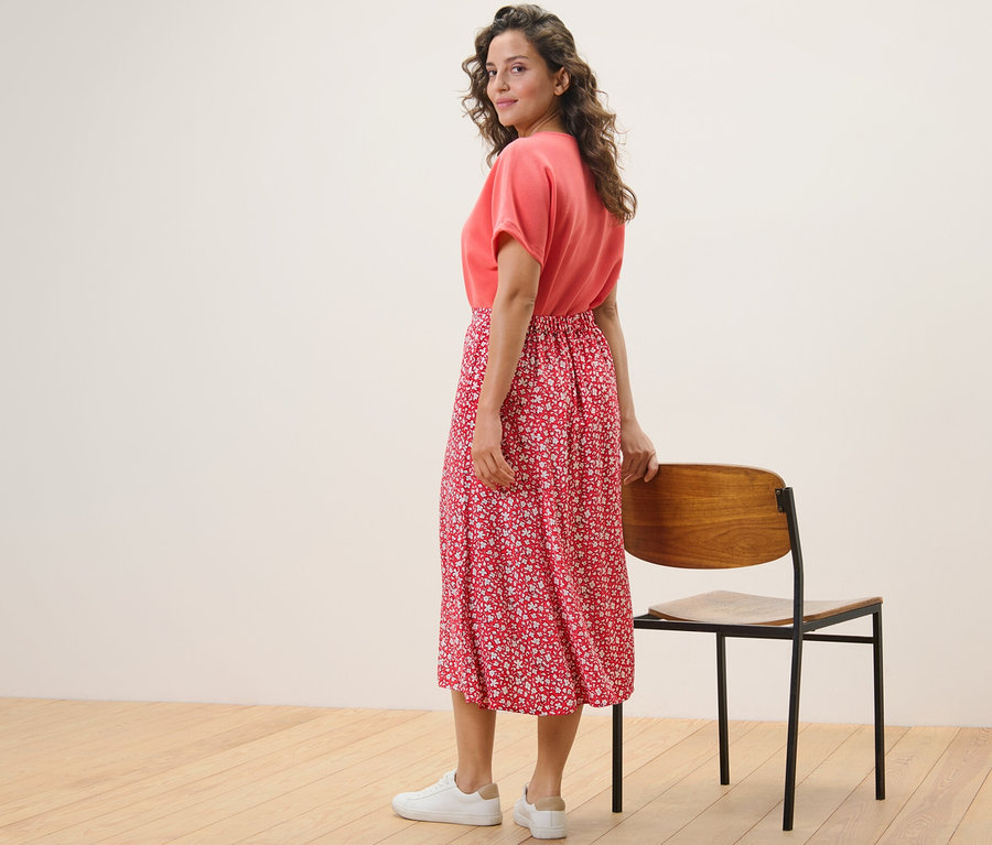 Eine Frau blickt über die Schulter und posiert in einem korallenfarbenen, bedruckten Midirock.