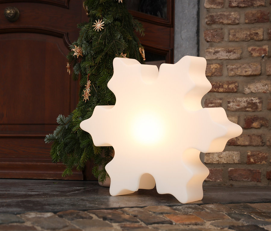 Eine leuchtende 60 cm LED-Schneeflocke von 8 seasons design steht neben einem kleinen Baum auf dem Boden.