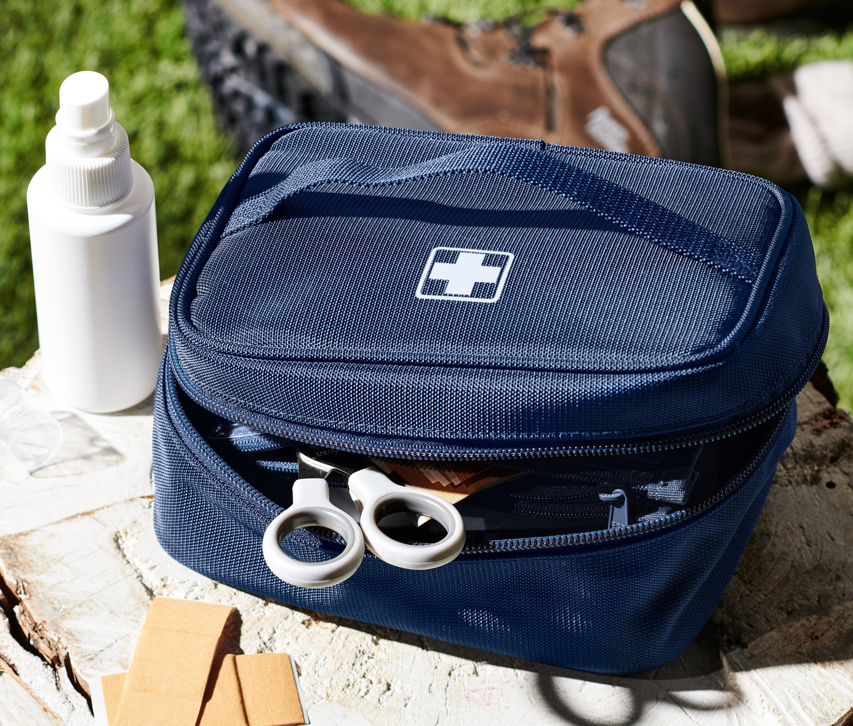 Eine blaue Medikamenten-Tasche mit weißem Kreuz auf einem Baumstumpf neben Spray, Pflaster und Schuhen.