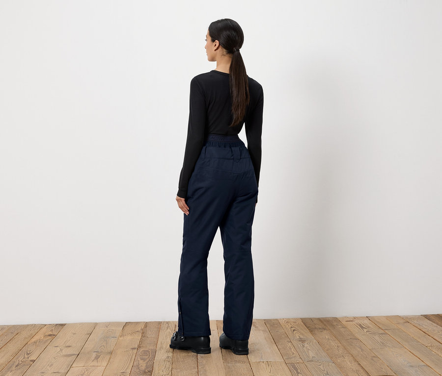 Frau steht mit dem Rücken zur Kamera und trägt ein schwarzes Langarmshirt und dunkelblaue Hosen.