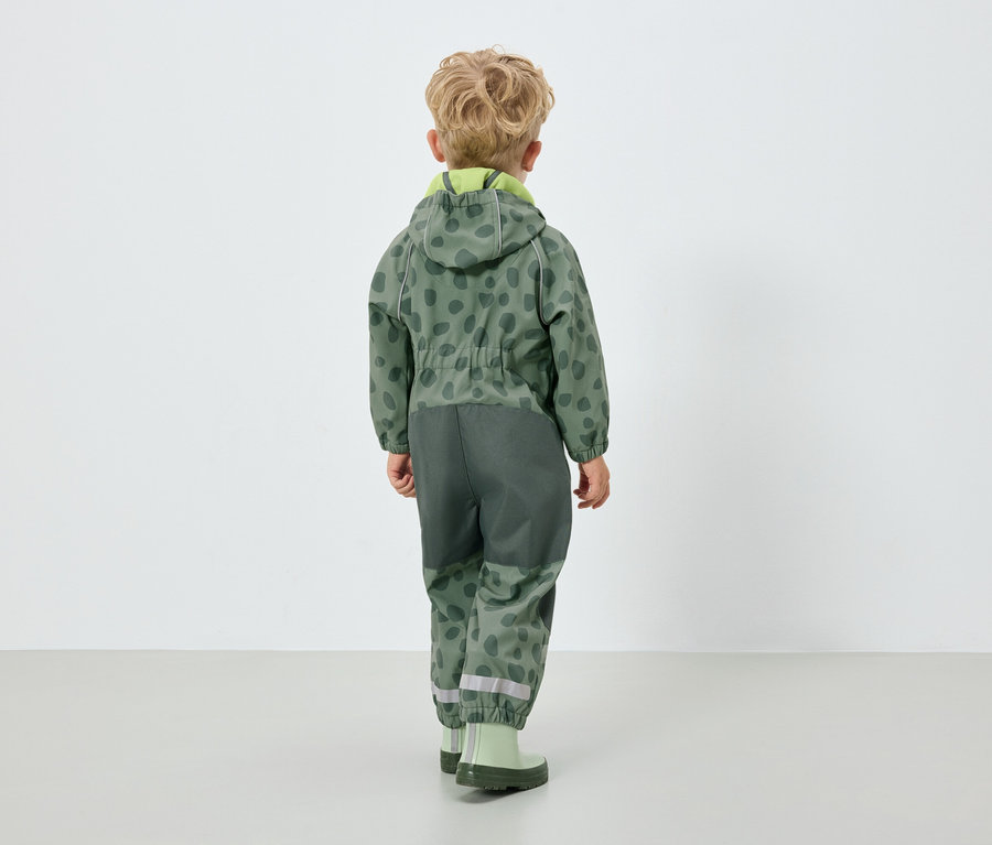 Junge in grünem Overall mit Kapuze, mit dem Rücken zur Kamera.