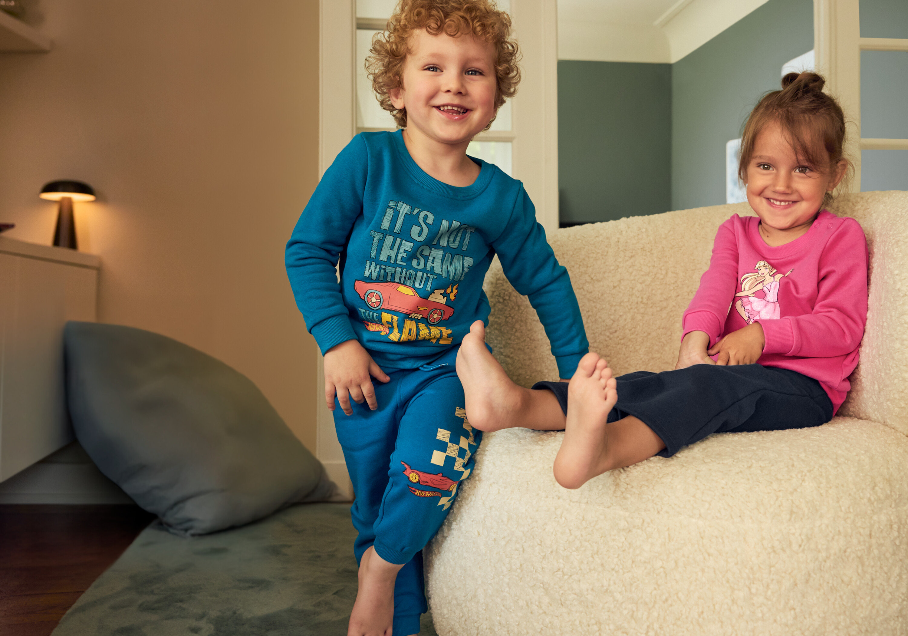Ein Junge im blauen Set und ein Mädchen im pinken Set sitzen auf einem beigen Sessel. Der Junge trägt 2 Flared Kinder-Thermoleggings mit angerauter Innenseite.