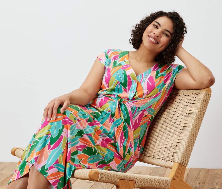 Frau sitzt in einem Stuhl und trägt ein Jerseykleid mit Knoten.