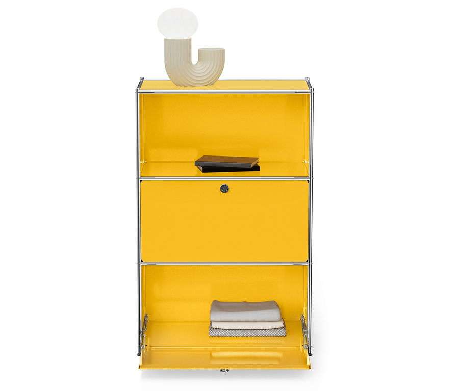 Gelber Schrank mit silbernem Rahmen, oben eine Lampe und ein Buch, unten gefaltete Handtücher.