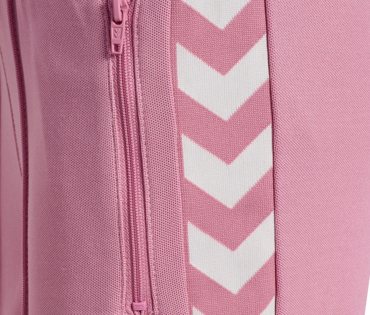 Detail einer rosafarbenen HUMMEL HMLJR Archive Wideleg Poly Pants mit weißen Chevrons und Reißverschlusstasche.