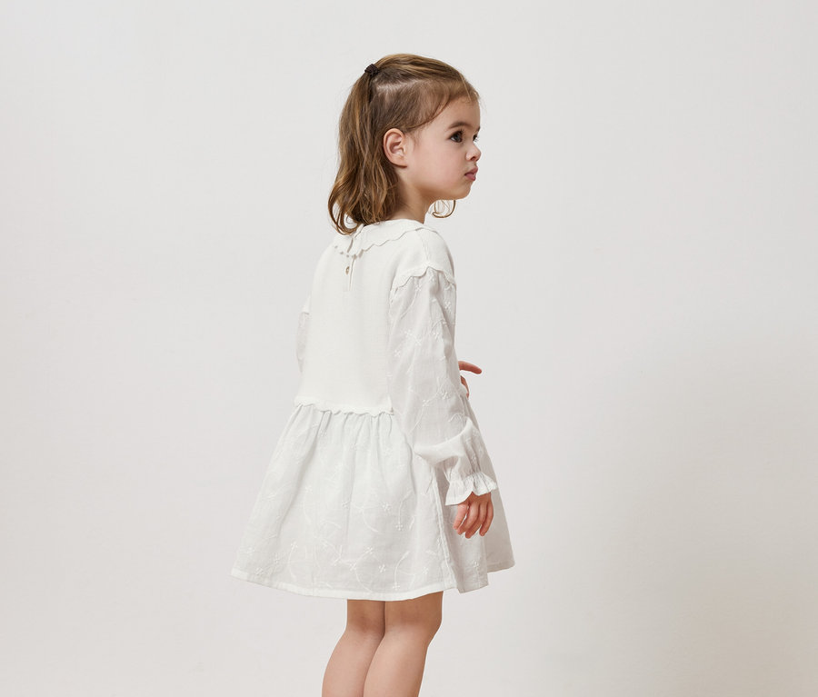 Mädchen in einem weißen Kleid mit langen Ärmeln und Rüschen.