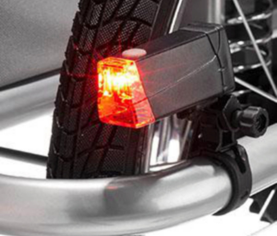 Rotes Fahrradrücklicht ist an einem silbernen Fahrradrahmen befestigt, mit einem Teil des Reifens im Hintergrund.