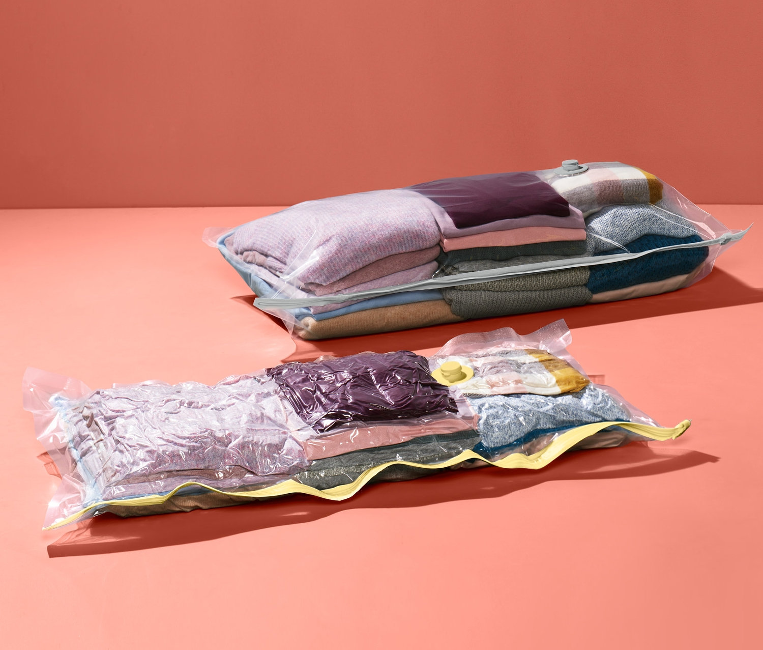Zwei Vakuum-Aufbewahrungsbeutel mit Kleidung auf korallenrotem Hintergrund.
