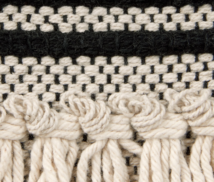 Detailaufnahme eines Makramee-Wandteppichs mit schwarzen und cremefarbenen Mustern.
