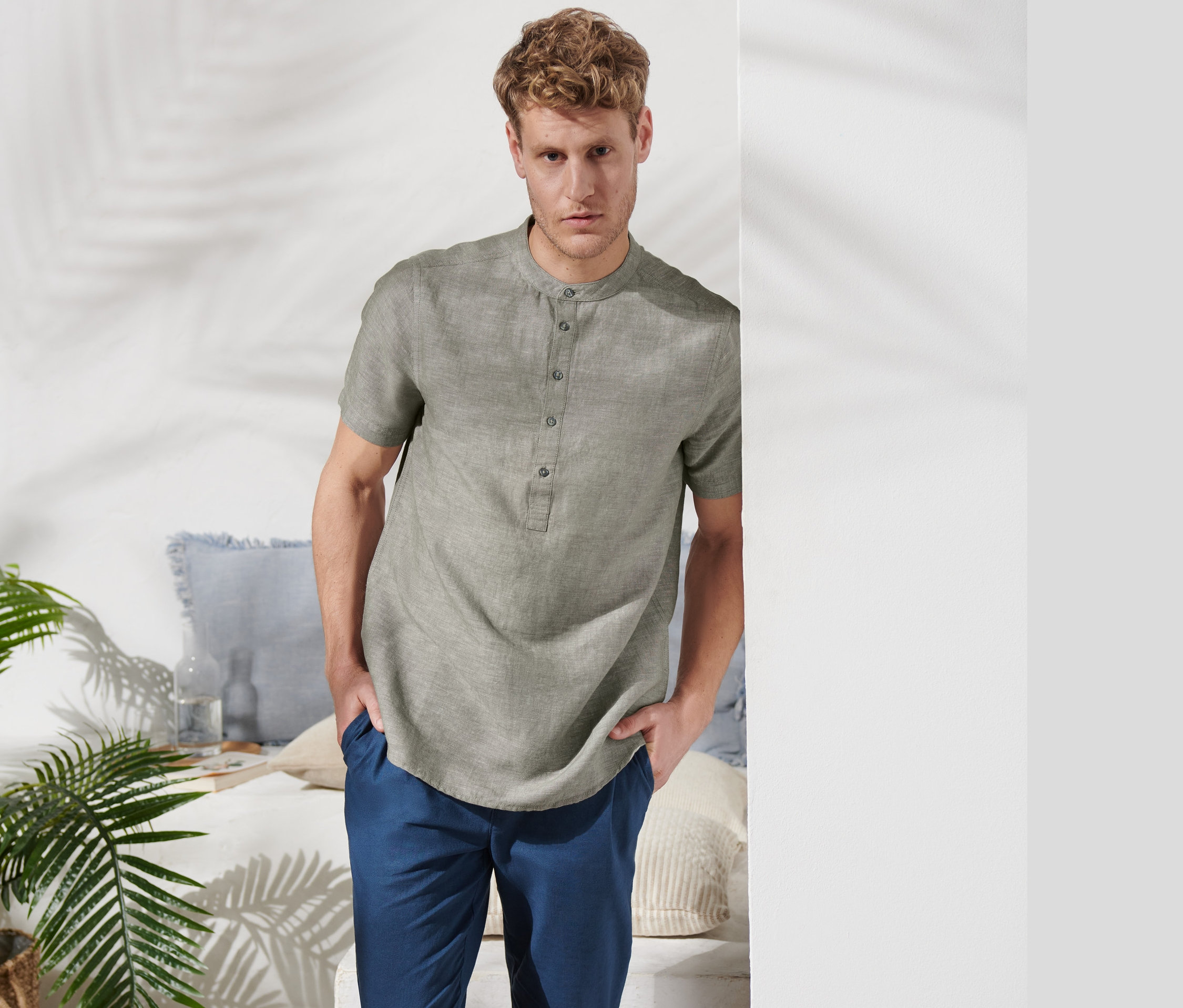 Mann posiert in einem khakifarbenen Kurzarmhemd mit Leinen und blauen Hosen.