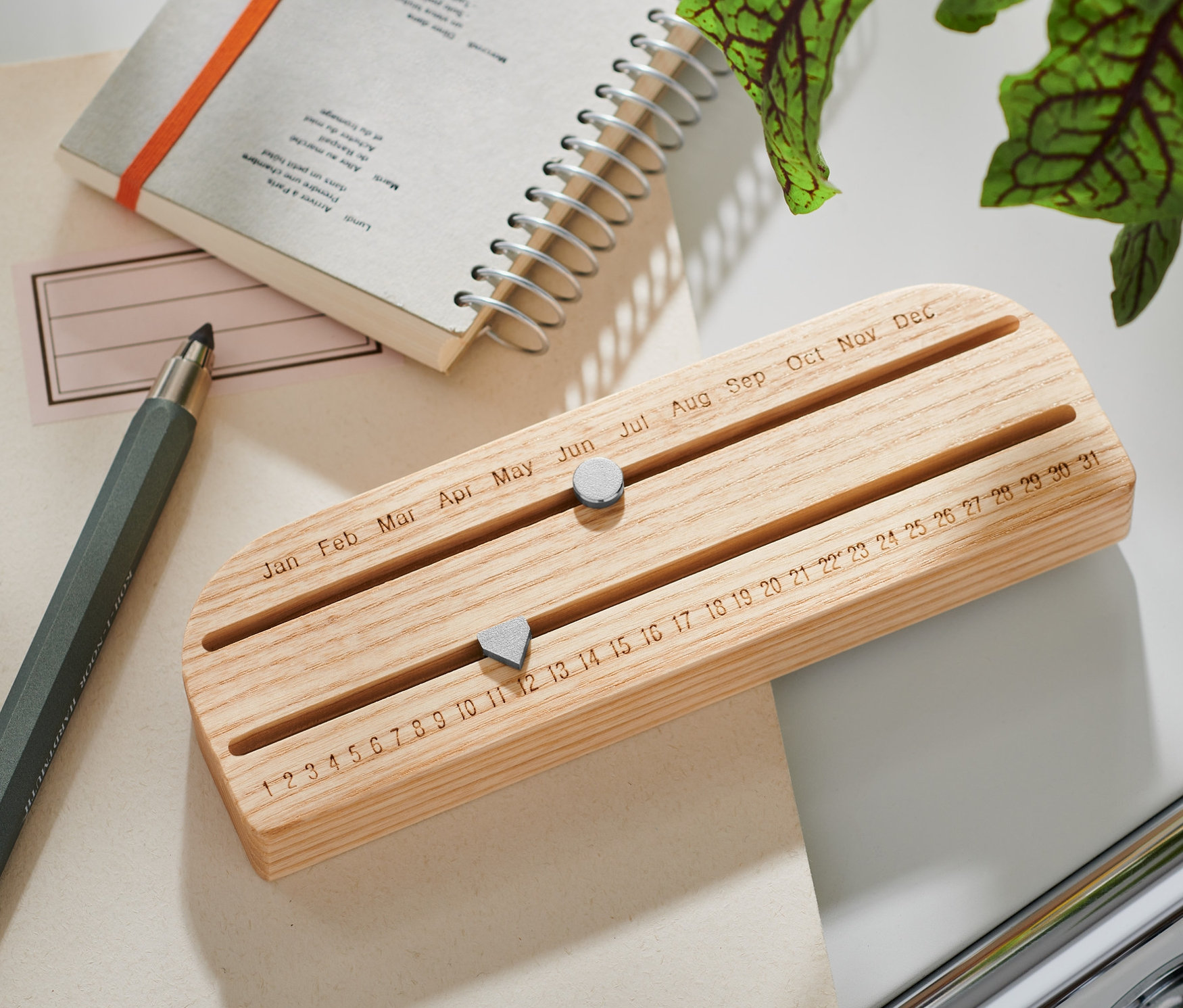 Ein Ewiger Kalender aus Holz liegt auf einem Tisch neben einem Block und einem Stift.