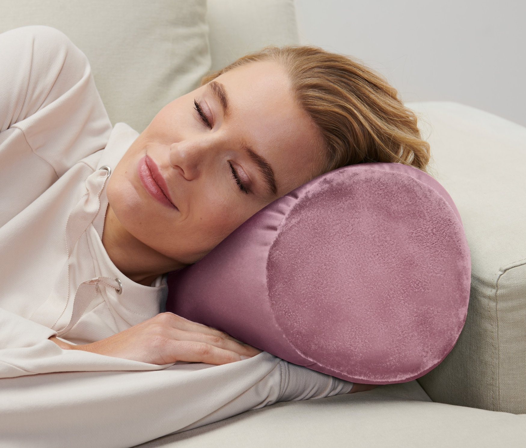 Frau schläft auf einem beigen Sofa mit einem Relaxkissen.