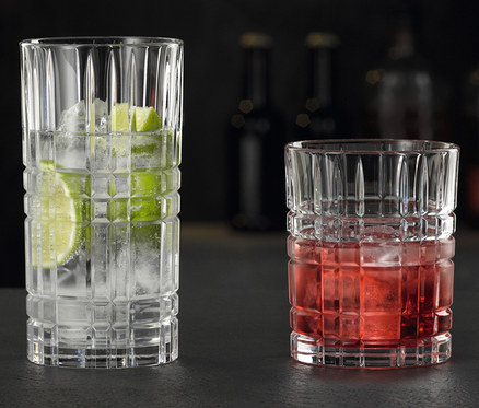 Zwei Gläser stehen auf einem Tisch. Links ein Longdrinkglas mit Eis und Limette, rechts ein Tumbler mit einem roten Getränk und Eis.