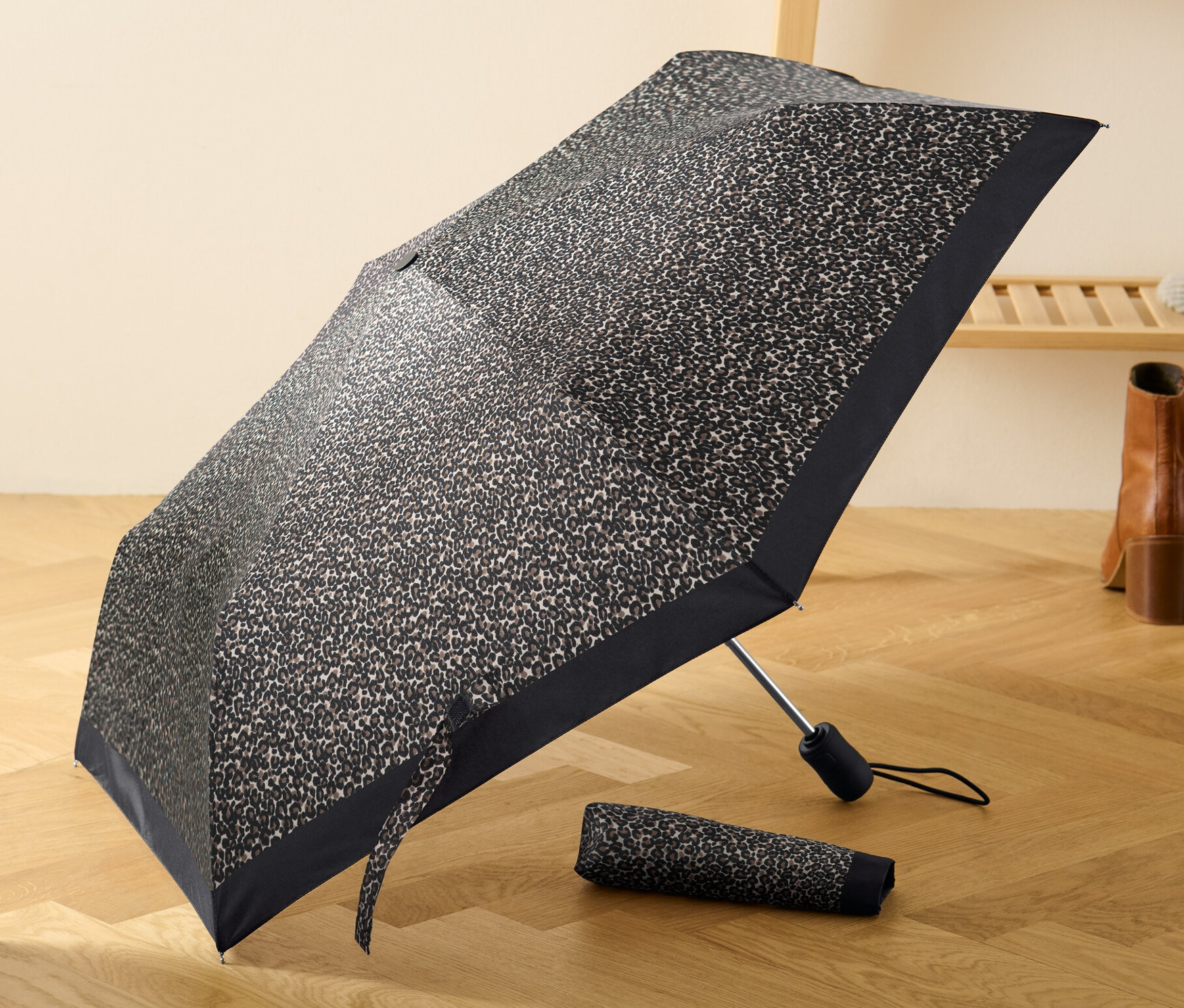 Geöffneter Automatik-Taschenschirm mit Leopardenmuster liegt auf einem Holzboden neben einem zusammengefalteten Schirm.