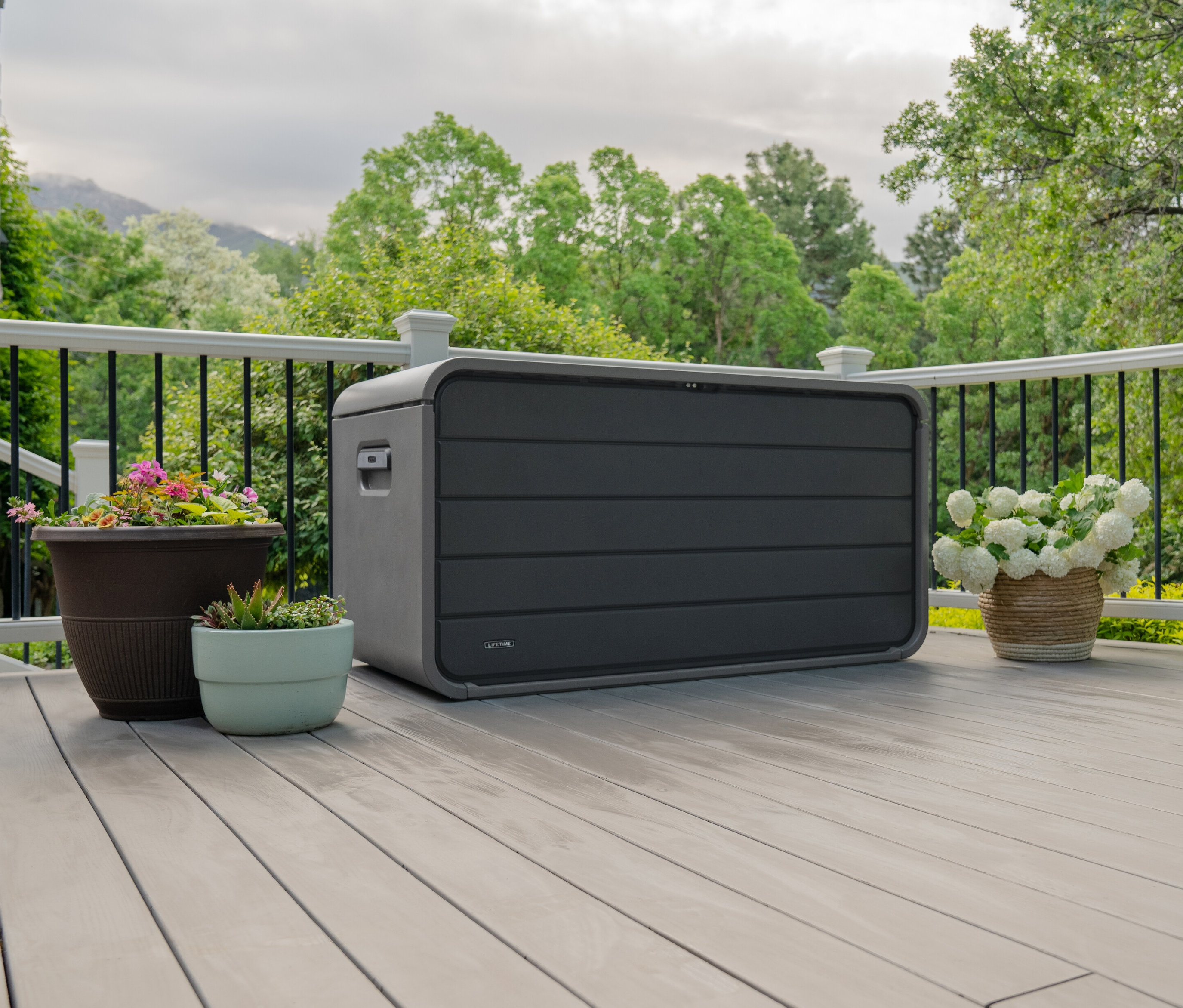 Graubraune Aufbewahrungsbox, 625 l, auf einer Terrasse neben Blumentöpfen.