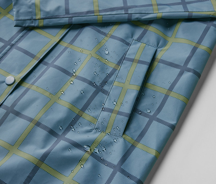 Detailaufnahme einer blauen Regenjacke mit Karomuster und Wassertropfen.